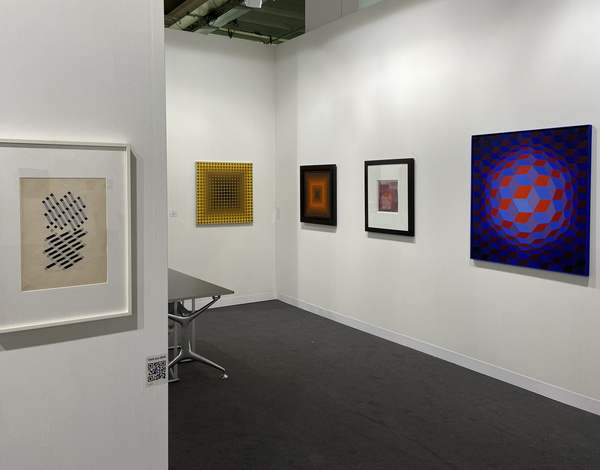 inside of small exhibition booth with paintings on white walls and dark grey event carpet