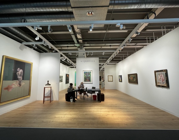 Painting exhibition stand in classic gallery style with wooden flooring and white walls, few people sitting in front of a framed painting