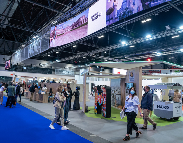 people walking between event hall stands inside big building with royal blue carpet pathway